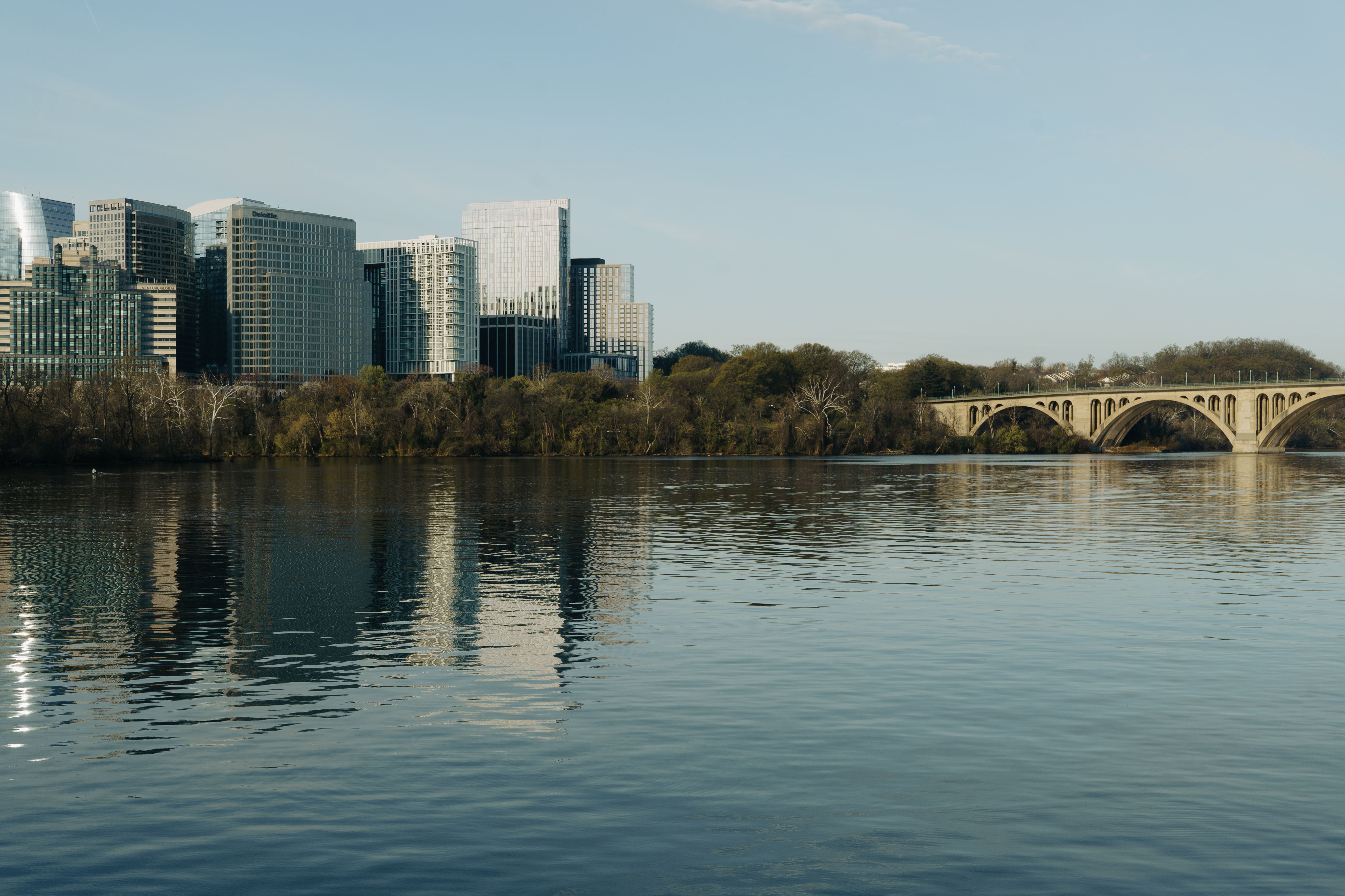 A scenic view of skyline buildings and Key Bridge reflecting on the Potomac River.
