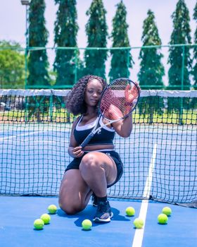 Confident woman with tennis racket on outdoor court surrounded by balls.