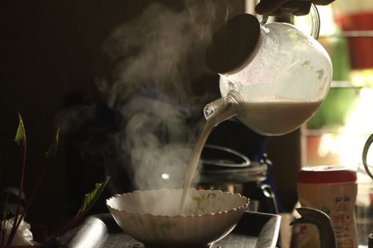 Warm morning light illuminates steaming milk being poured into a bowl.