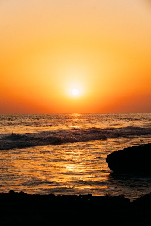 Free A breathtaking sunset casting golden hues over the ocean and rocky shoreline, creating a serene natural scene. Stock Photo