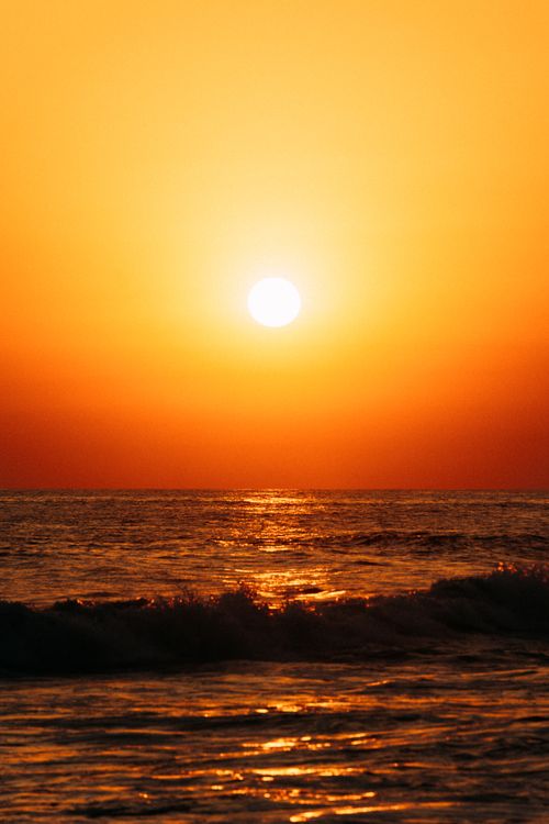 Free Golden sun setting over ocean waves, casting an orange glow across the horizon. Stock Photo