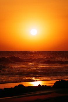 A breathtaking sunset over ocean waves creates a serene twilight landscape on the beach.