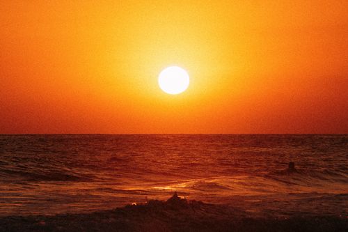 Free A stunning orange sunset over the ocean, featuring a surfer silhouetted against the waves. Stock Photo