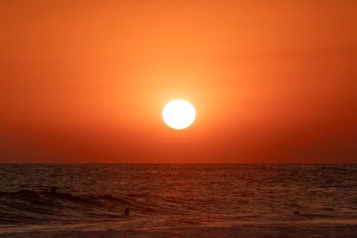 Free Captivating ocean sunset with a vibrant orange sky and the sun dipping below the horizon. Stock Photo