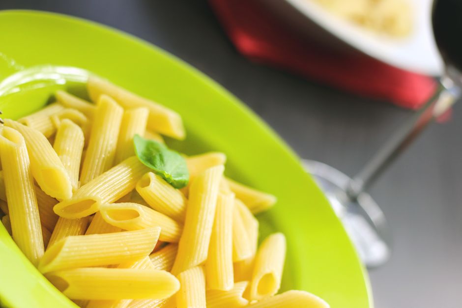 Close-up of penne pasta topped with basil, elegantly served on a lime green plate.