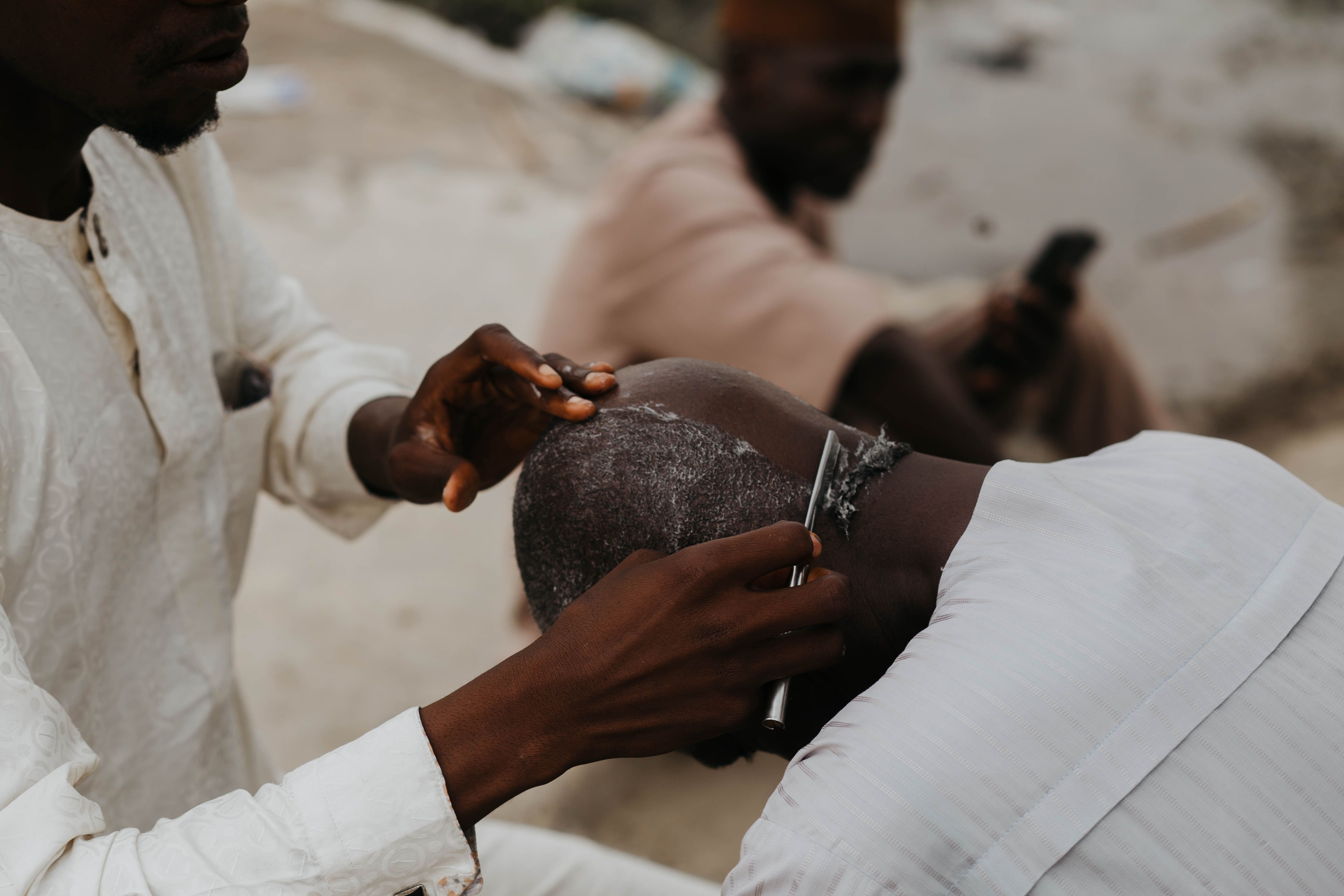 A street barber skillfully shaves a customer's head outdoors. Captures a cultural moment.