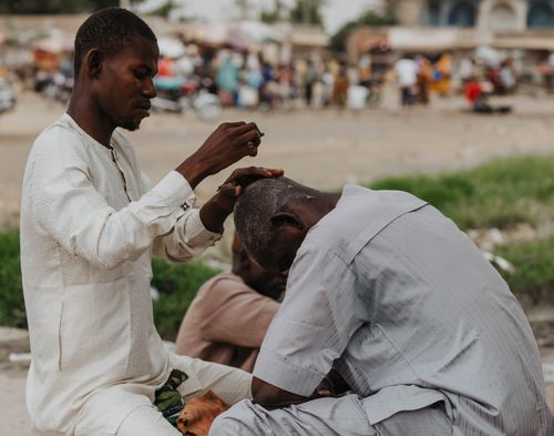 Free Outdoor scene of a barber cutting hair in a bustling street setting. Stock Photo