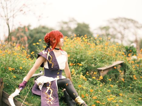 A cosplayer dressed in a costume sits serenely in a field of vibrant flowers, enjoying a peaceful moment.