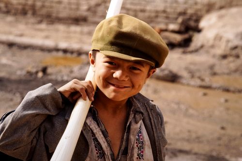 Free Smiling young boy holding a pipe in a rural Chinese setting, wearing a cap and jacket. Stock Photo