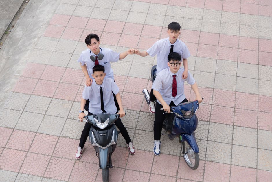 Four young men in school uniforms posing on scooters, showing camaraderie.