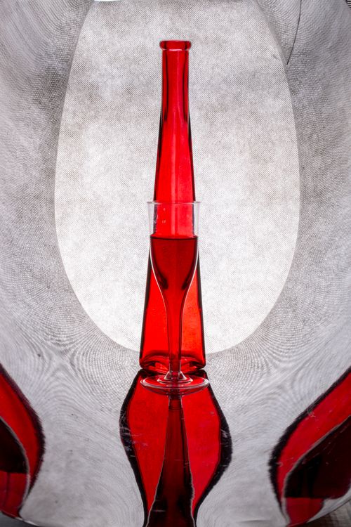 Free A red glass bottle on a reflective surface creates vibrant abstract patterns. Stock Photo