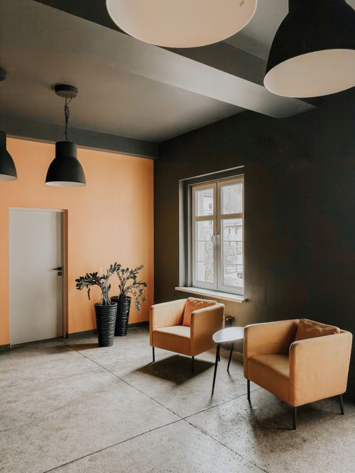 Free A modern indoor lounge with minimalist design featuring orange chairs and black accents, perfect for office ambience. Stock Photo