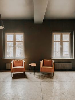 Two armchairs and a table in a serene, sunlit minimalist room with two large windows.