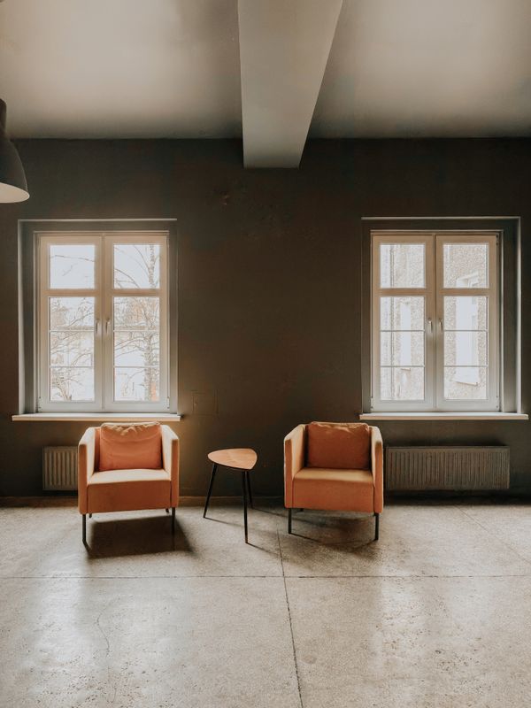 Two terracotta armchairs between tall windows, by Luk Sauvage on Pexels