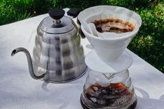 A pour-over coffee setup with a kettle and dripper on a sunny outdoor table.