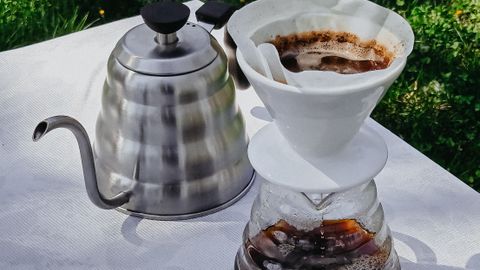 A pour-over coffee setup with a kettle and dripper on a sunny outdoor table.