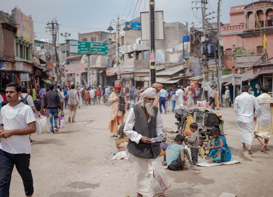 A vibrant street in Varanasi with people, shops, and colorful buildings, showcasing local culture.