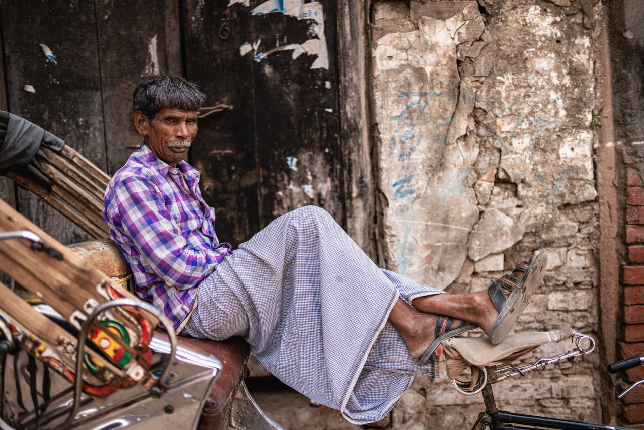 a man in traditional attire sits relaxed on a rickshaw against a rusti