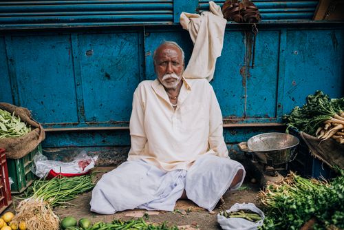 Free Portrait of an elderly vendor selling fresh produce at a bustling market in Varanasi, India. Stock Photo