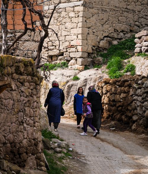 Free A heartwarming village scene capturing locals walking along a cobblestone path, surrounded by rustic stone walls. Stock Photo