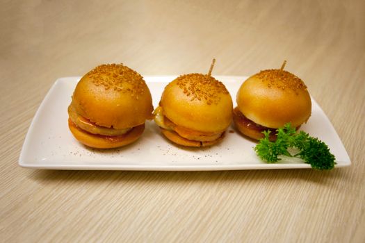 Three mini burgers presented on a white rectangular plate with parsley garnish.