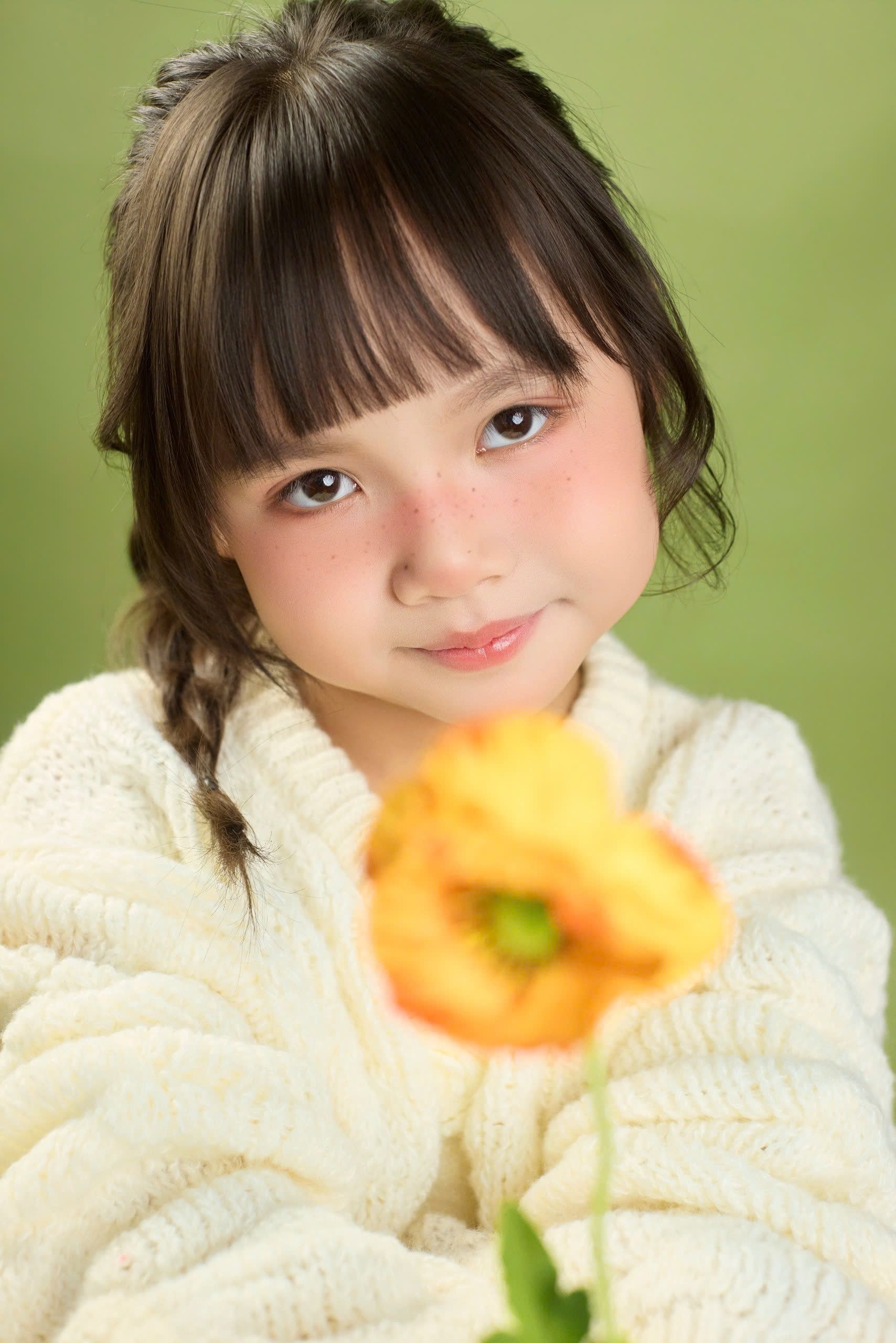 Portrait of a young girl smiling, holding a poppy flower against a green backdrop.