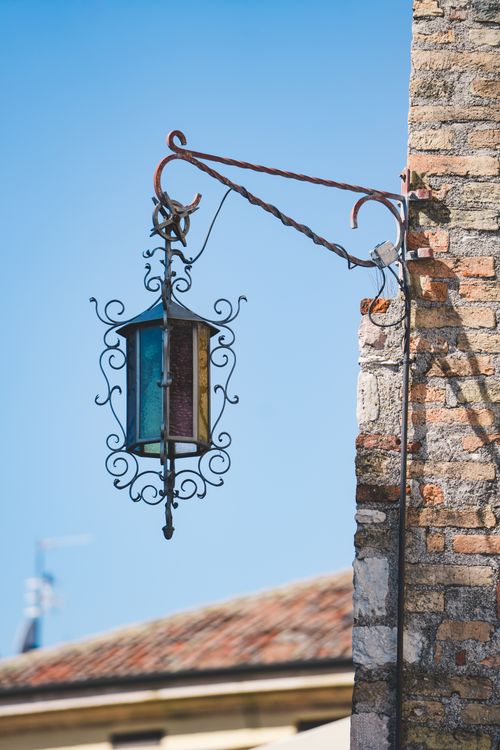 Free Beautiful antique lantern hangs on a rustic wall against a clear blue sky in Riva del Garda, Italy. Stock Photo