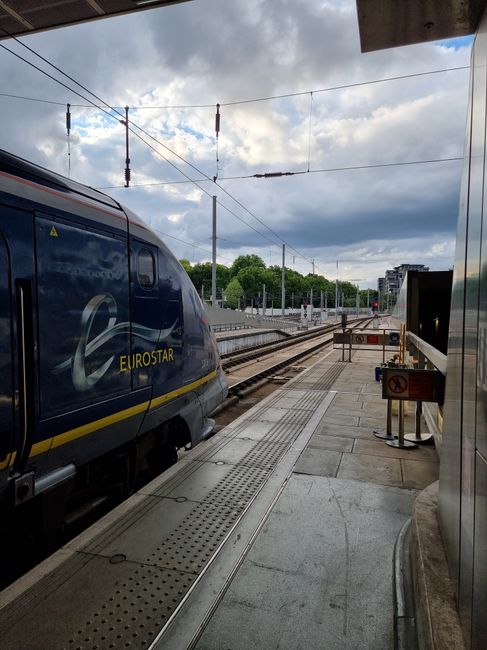 Eurostar train at a Paris station platform, featuring rails leading into the distance under a cloudy sky.