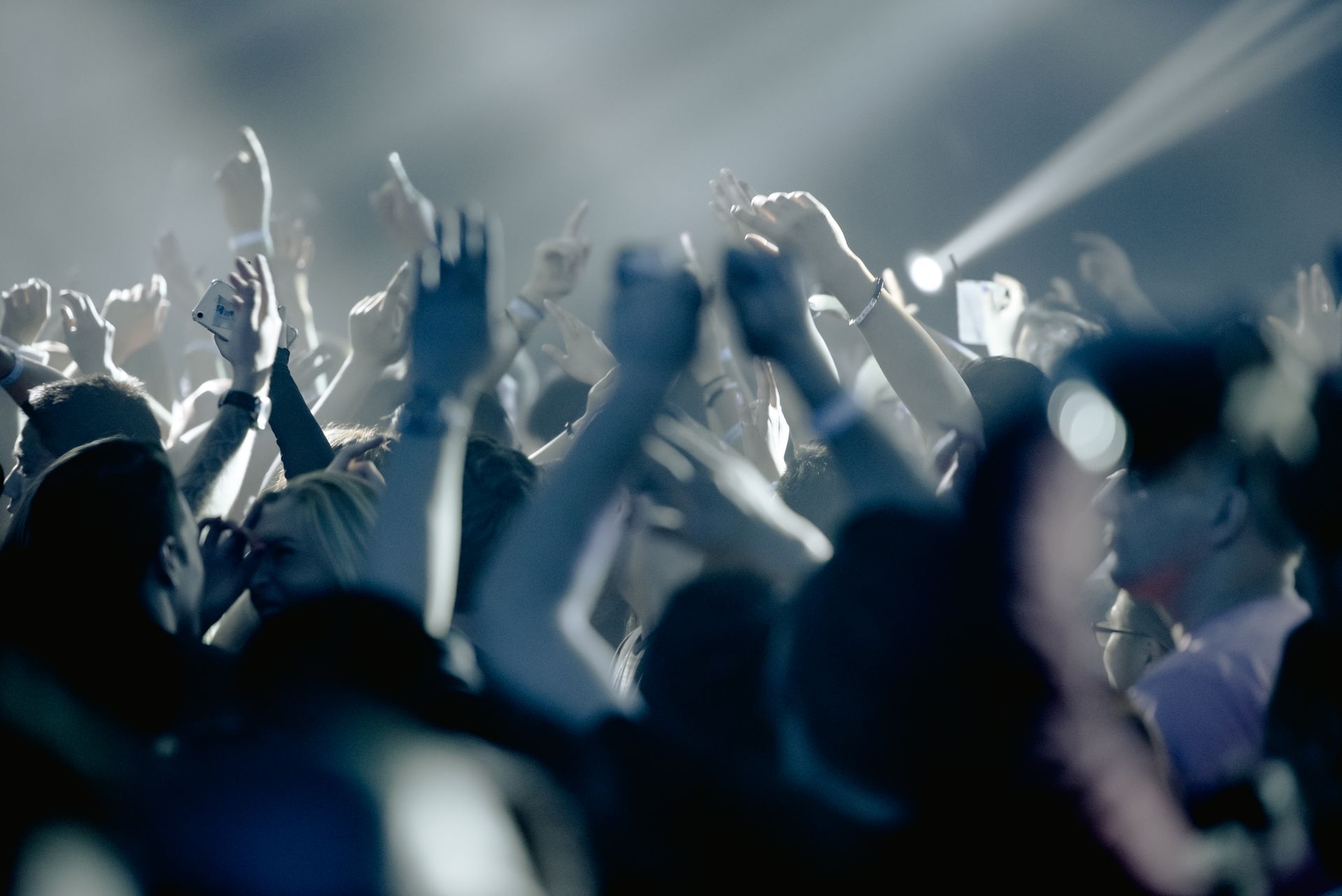 Thrilled people raising hands in excitement and cheering during live concert in dark club