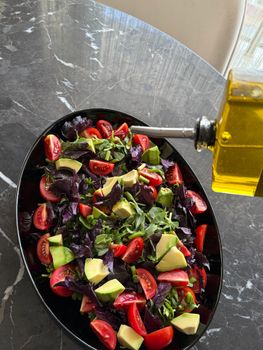 Delicious Mediterranean salad with cherry tomatoes, avocados, and leafy greens, drizzled with olive oil.