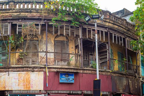 Free A worn colonial-style building with fading shutters and lush overgrowth in an urban area. Stock Photo