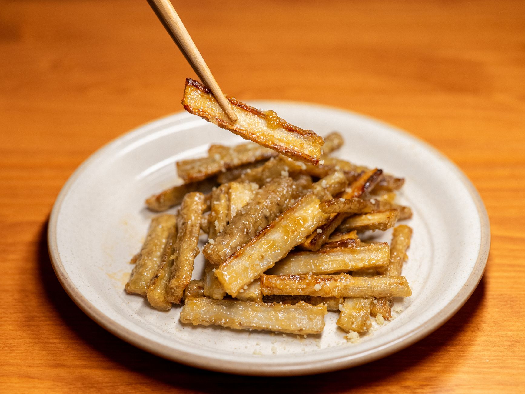 Delicious crispy fried burdock root served on a white plate with chopsticks.