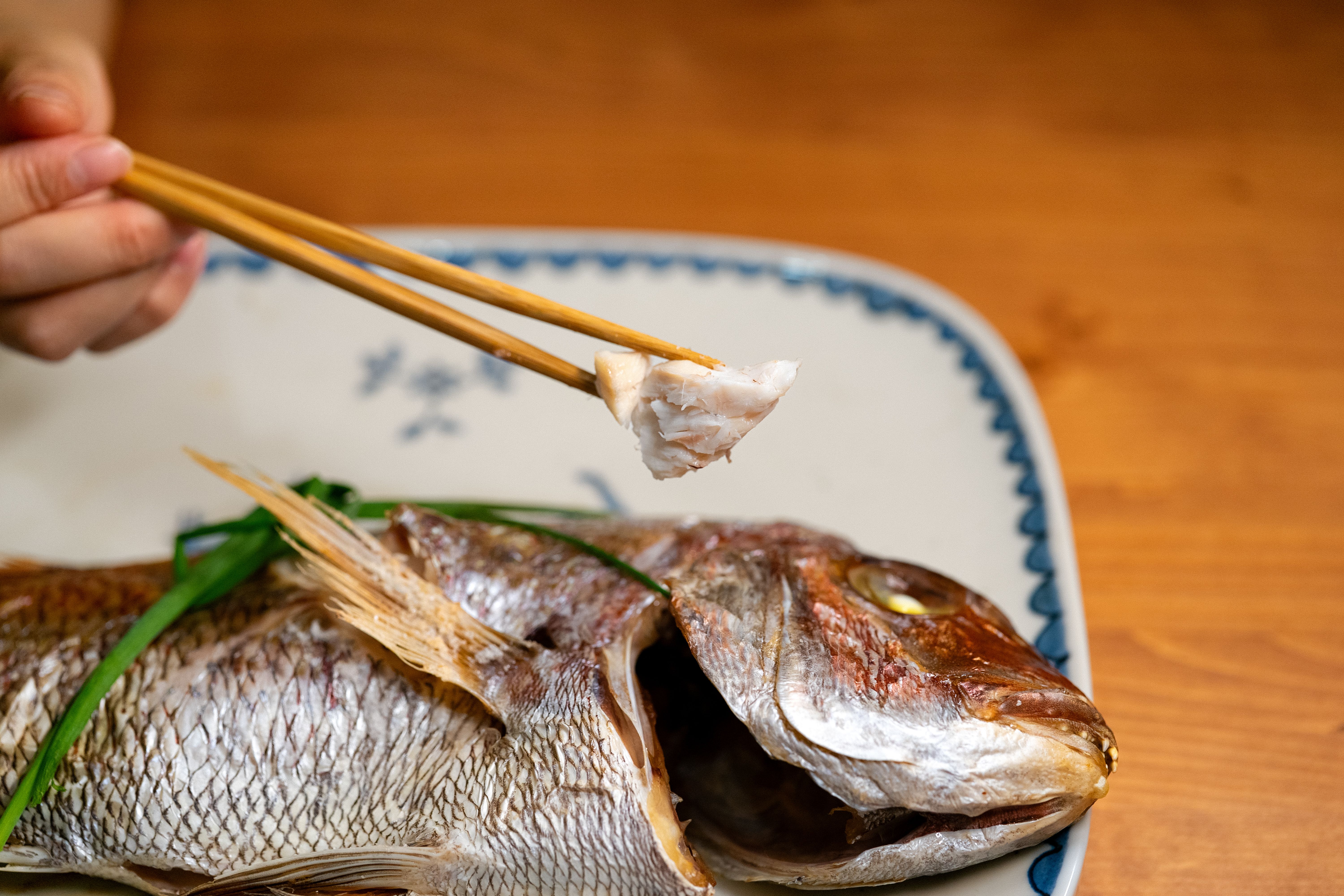 A close-up of a traditional Asian grilled fish served on a decorative plate with chopsticks. | BocaVibe
