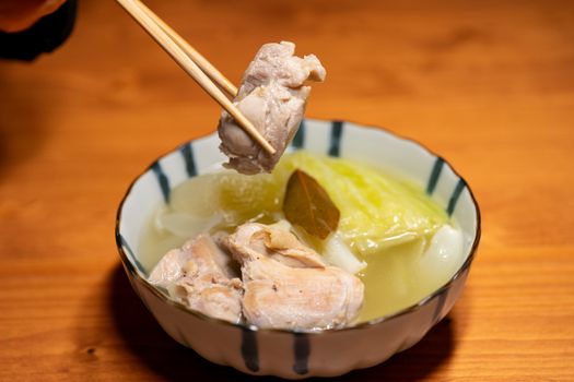A bowl of Asian cuisine with boiled vegetables and meat, held with chopsticks.