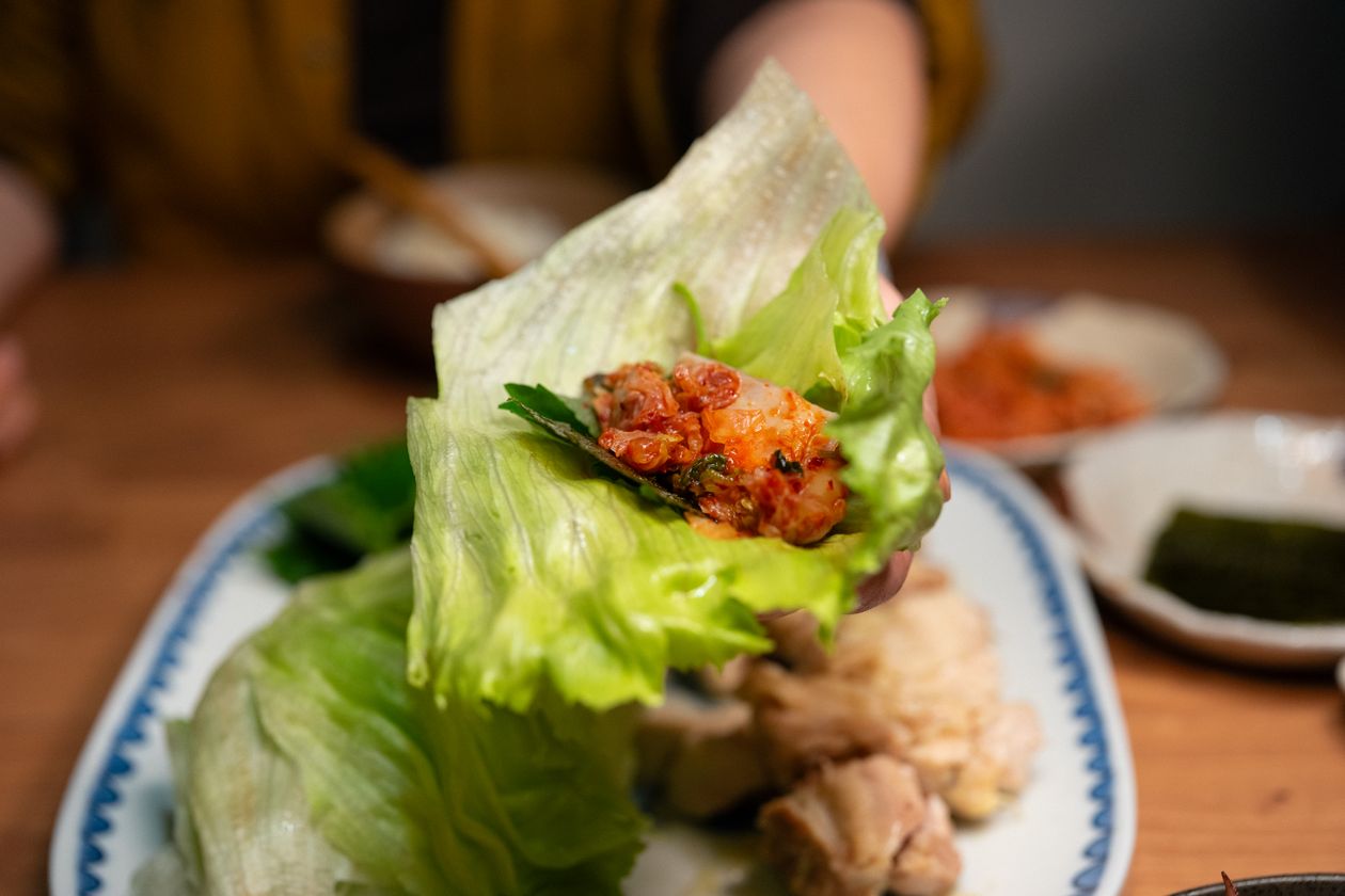 Close-up of a Korean-style lettuce wrap filled with rice, meat, and kimchi, held in a lettuce leaf