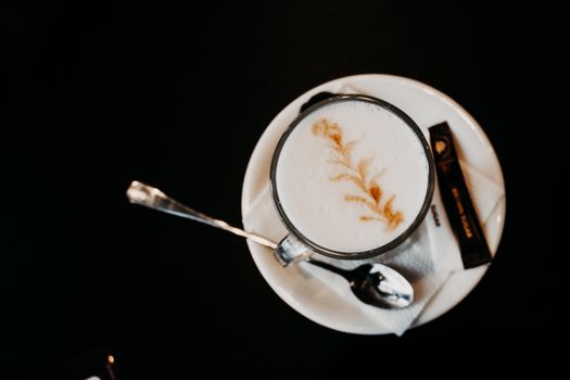 Overhead shot of a cappuccino with artistic latte foam design alongside a spoon on a saucer.
