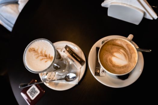 Overhead view of two lattes with artistic foam art, placed on a wooden table.