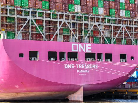 A large pink container ship named ONE Treasure docked in Panama for cargo loading.