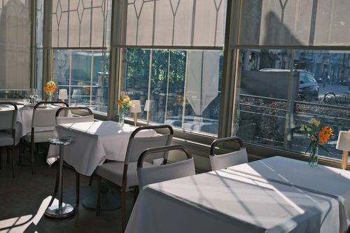 Free Charming bright restaurant interior with sunlight, tables, and vibrant flower arrangements. Stock Photo