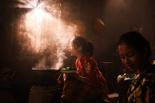 Free Two women in traditional attire cooking in a softly lit room with warm steam rising. Stock Photo