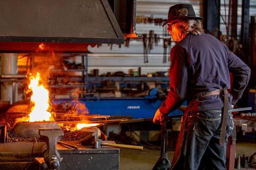 Blacksmith crafting metal with fire in an industrial workshop setting.
