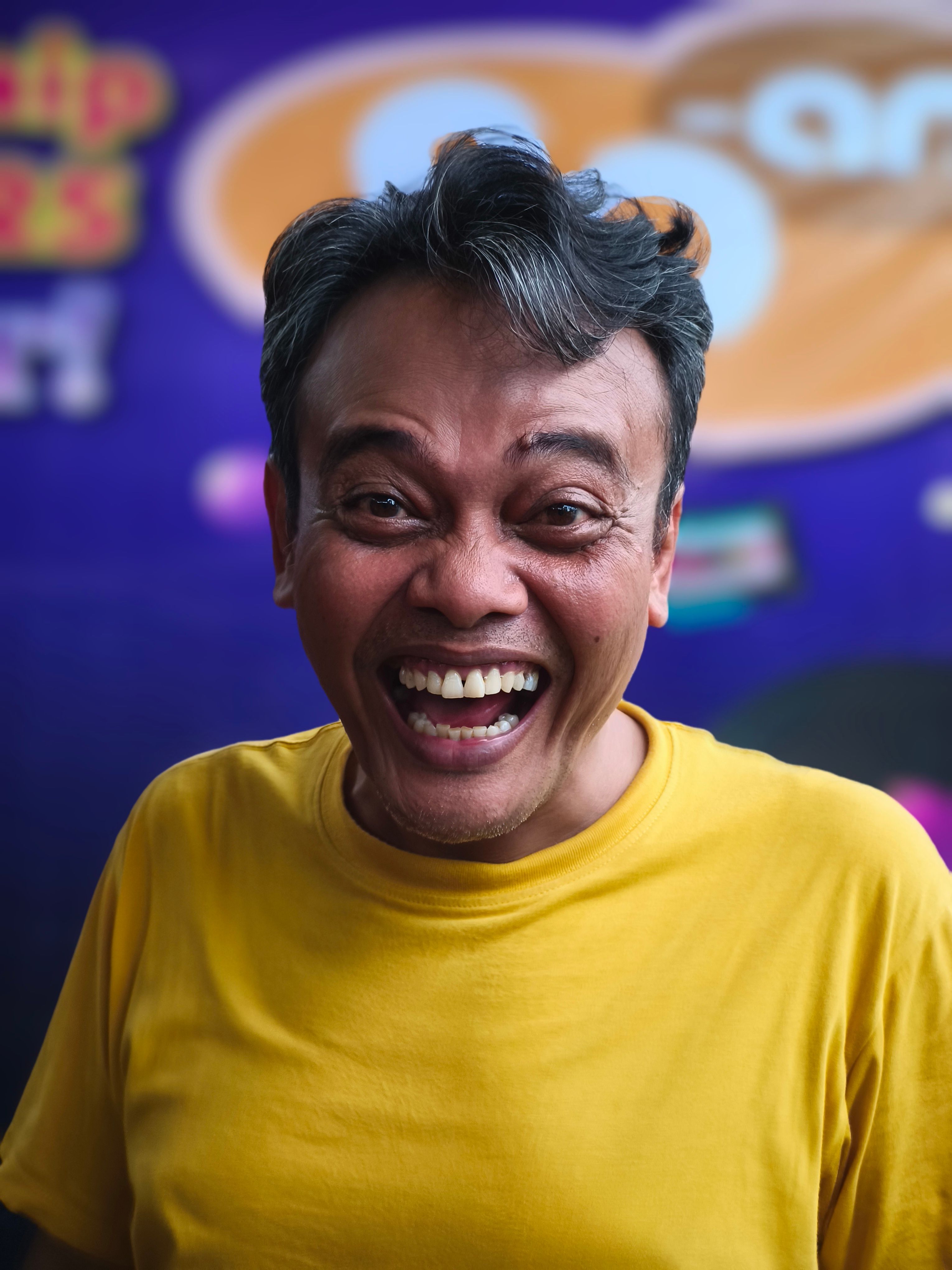 Cheerful man laughing in a yellow shirt with a colorful blurred background.