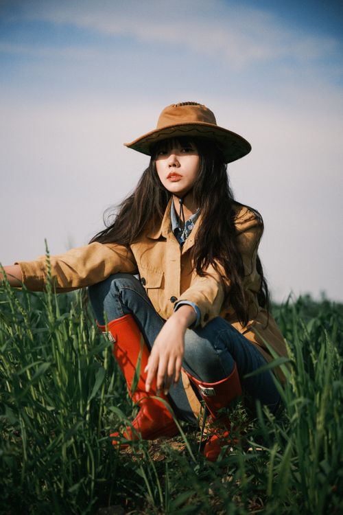 Free Portrait of a woman in a field wearing a wide-brimmed hat and red boots, symbolizing rural lifestyle. Stock Photo