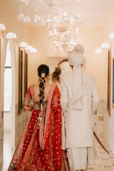 Elegant photo of a bride and groom in traditional attire walking down a beautifully decorated hallway.