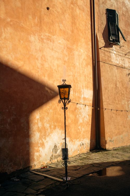 Free A vintage lamp post casting a shadow on a textured wall in the afternoon sun. Stock Photo