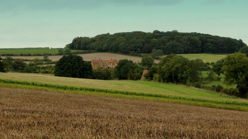 Free Idyllic countryside scene with farmhouse surrounded by fields and trees under a cloudy sky. Stock Photo