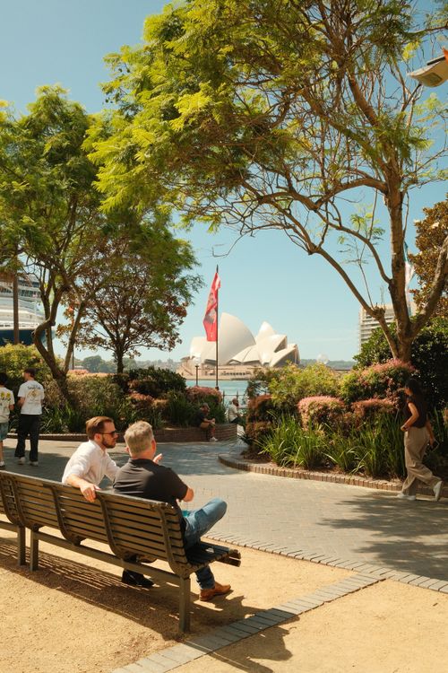 Free Visitors enjoy a sunny day at Sydney Botanical Gardens with the iconic Sydney Opera House in the background. Stock Photo
