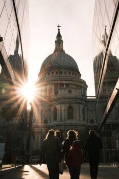 Dramatic sunset view of St Paul's Cathedral, London, with silhouettes of people and modern reflections.