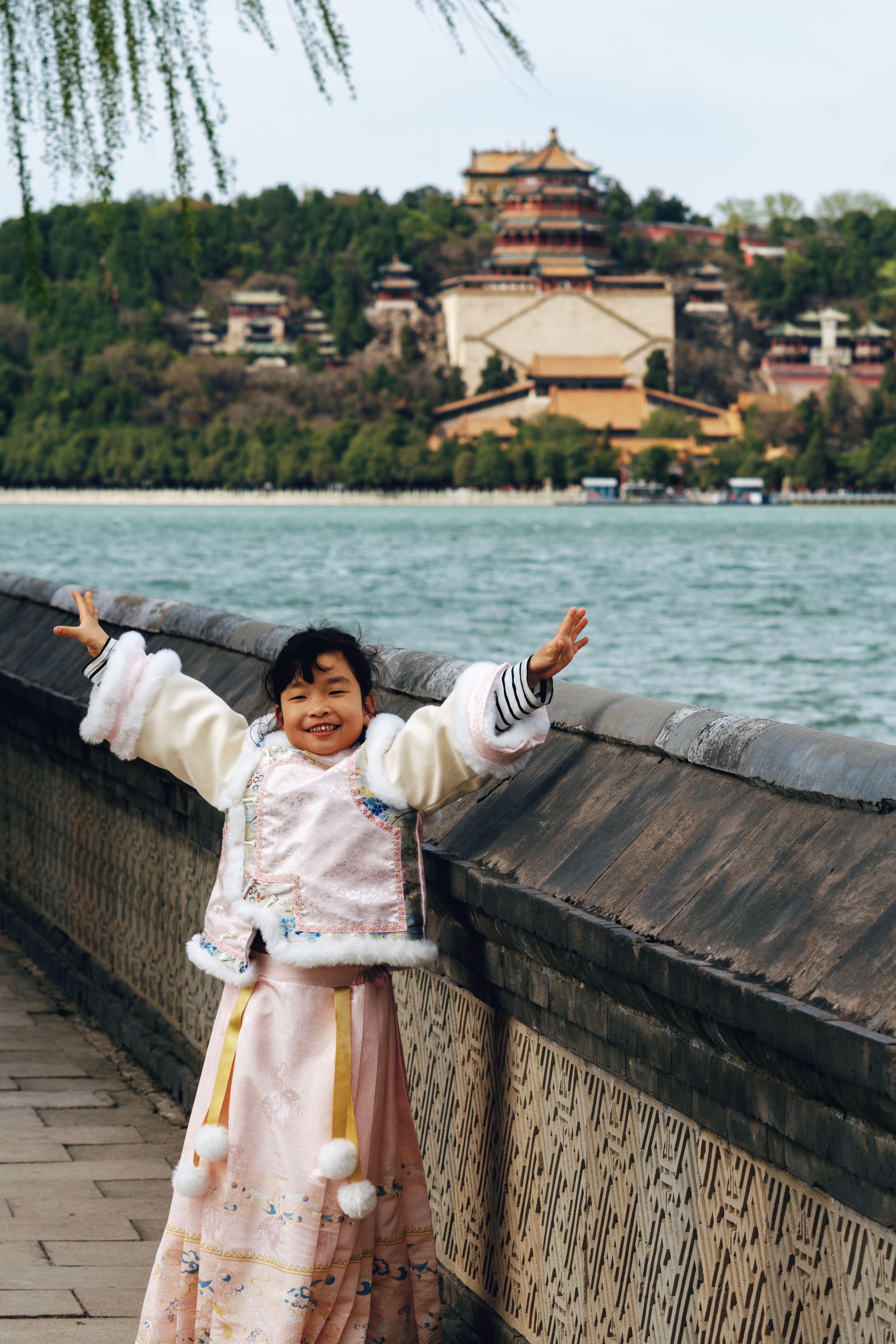 A cheerful child in traditional attire enjoying the scenic view at Beijing's Summer Palace.