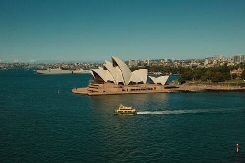 Free A scenic view of Sydney Opera House with vibrant harbor activity and city skyline in the background. Stock Photo